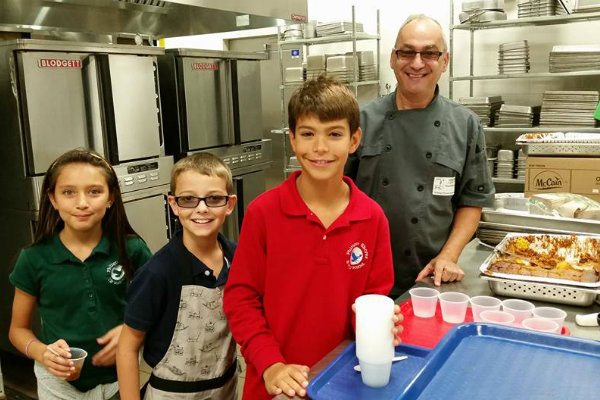 kids in cafeteria kitchen learning to cook from chef