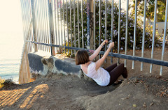 Woman sliding under hole beneath a metal fence